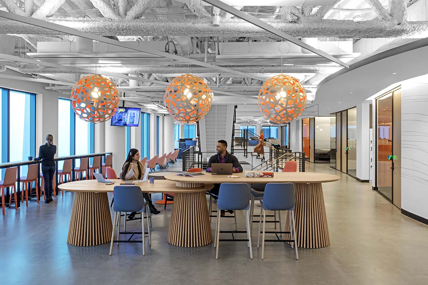 Open collaboration tables with orange globe pendants and blue chairs