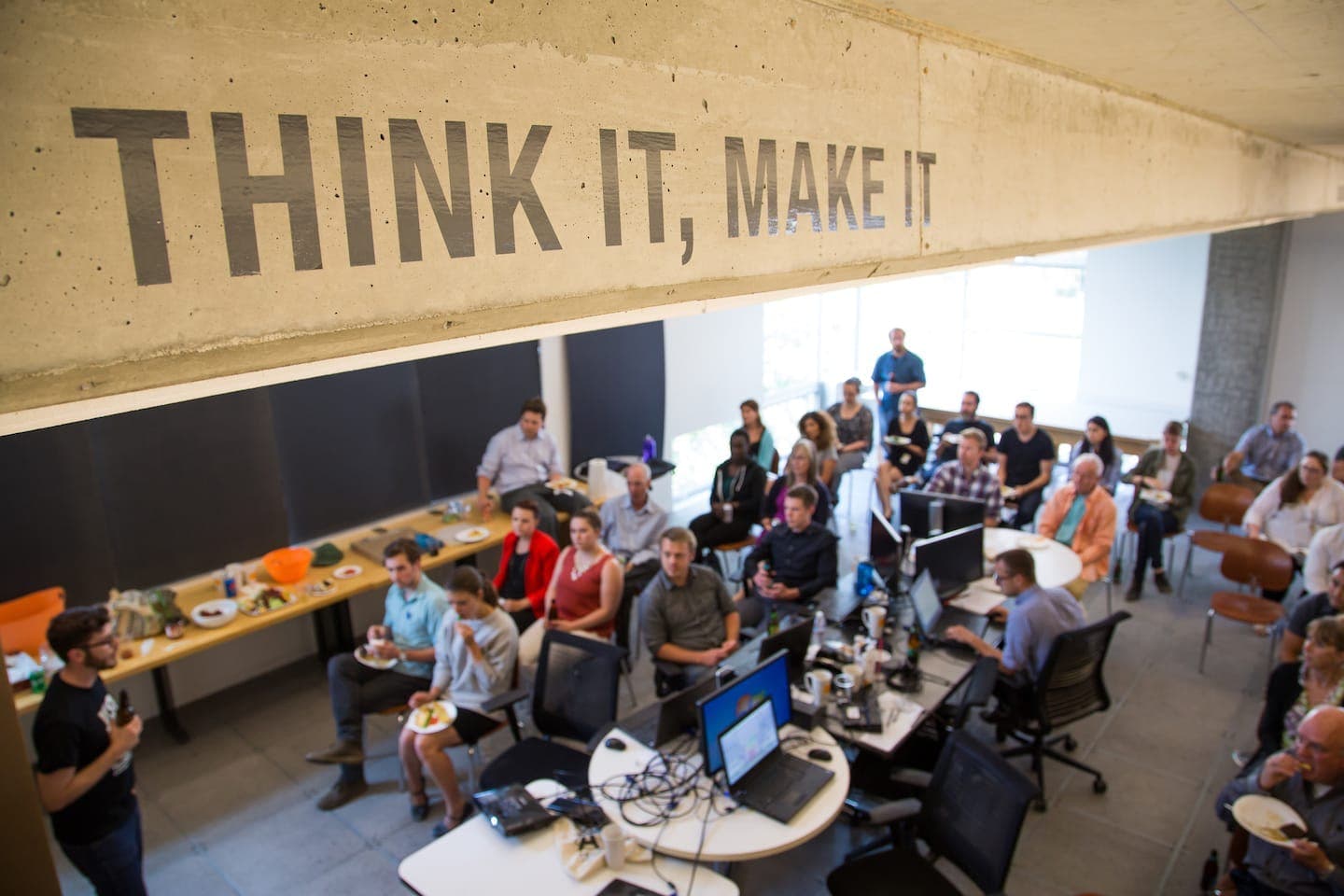 Hackathon audience under a concrete beam painted with the words Think It, Make It