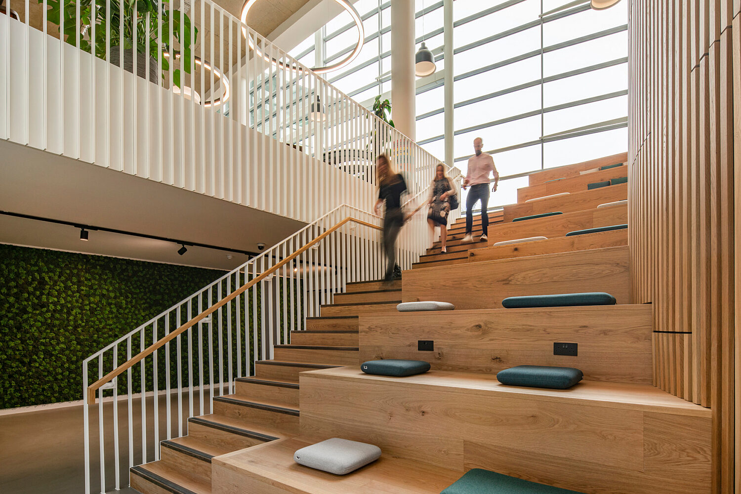 Bespoke timber staircase with teal cushioned seating steps inside a bright atrium with a living moss wall